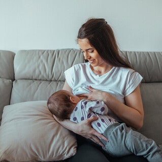 Mamá sentada en un sofá sonriendo, amamantando a su bebé. Lactancia materna.
