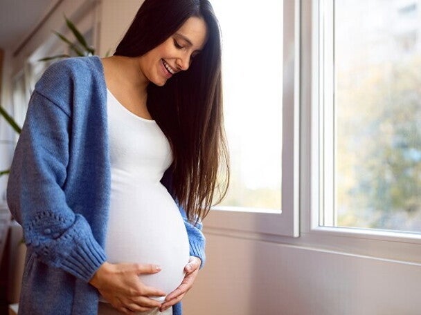 Mujer embarazada vestida de blanco, sonriendo y sosteniendo su vientre con las manos