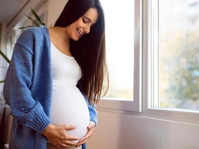 Mujer embarazada vestida de blanco, sonriendo y sosteniendo su vientre con las manos