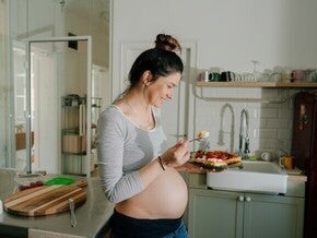 Mujer embarazada sonriendo en la cocina comiendo antojo dulce