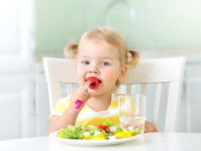 Pequeña comiendo verduras durante la comida.