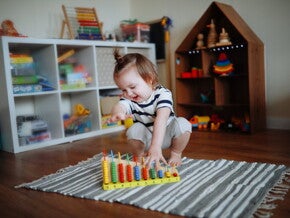 Niña de dos años jugando sobre la alfombra con ábaco de madera. Juego tranquilo como rutina diaria.