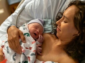 Mamá abrazando a su bebé en una cama de hospital luego de un parto por cesárea