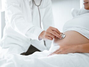 Mujer embarazada acostada en cama de hospital. Doctor con un estetoscopio escucha los latidos del bebé. Etapas de parto.