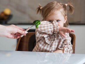 Mamá está alimentando a una niña brócoli con cuchara. La bebé se niega a comer. 