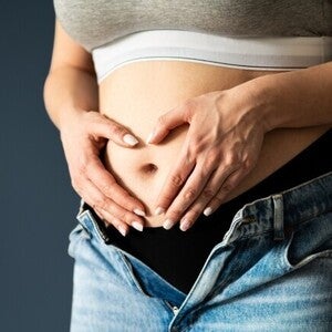 Abdomen de mujer embarazada en primer o segundo trimestre, manos en forma de corazón sobre el vientre.