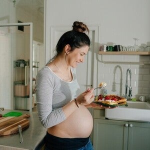 Mujer embarazada sonriendo en la cocina comiendo antojo dulce