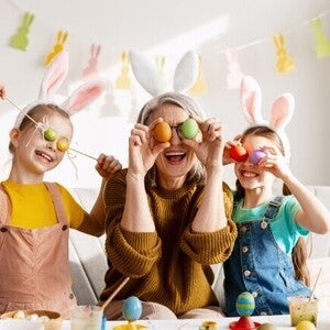 Padres y niños celebrando Pascua, cubriendo sus ojos con huevos de colores de forma divertida.