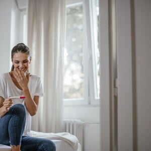 Mujer sentada en la cama sonriendo y mirando un test de embarazo