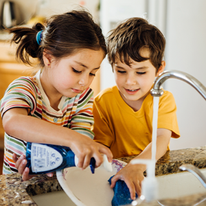 Niña y niño lavando un plato en la cocina.