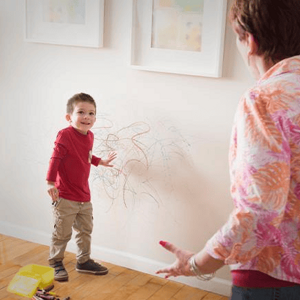 Niño con dibujos de crayón por la pared y un adulto reaccionando.