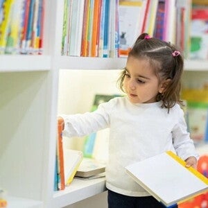 Beneficios de HMOs y probióticos para el sistema inmune Niña pequeña buscando libros en una biblioteca infantil.