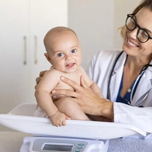 Doctora sonriendo y pesando a un bebé feliz.