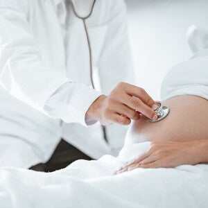 Mujer embarazada acostada en cama de hospital. Doctor con un estetoscopio escucha los latidos del bebé. Etapas de parto.