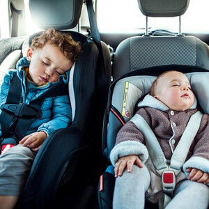 Niño pequeño y bebé durmiendo cada uno en una silla de seguridad para el auto.