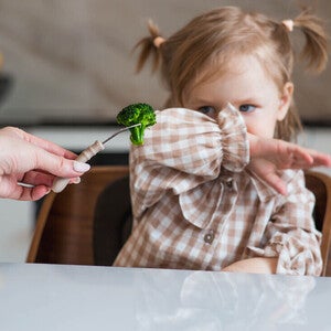 Mamá está alimentando a una niña brócoli con cuchara. La bebé se niega a comer. 