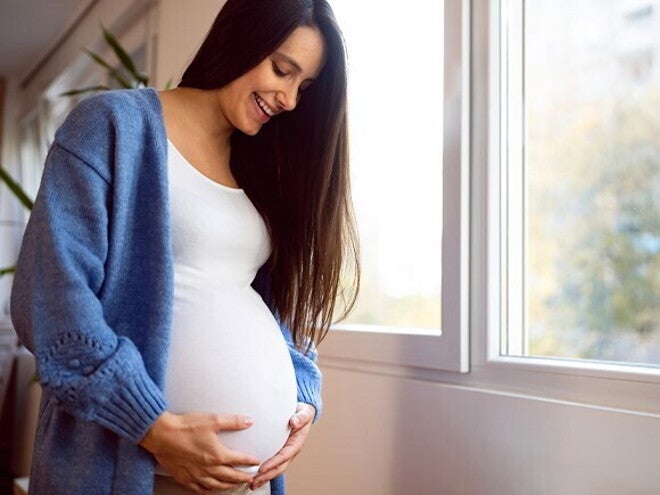 Consejos para un embarazo saludable Mujer embarazada vestida de blanco, sonriendo y sosteniendo su vientre con las manos
