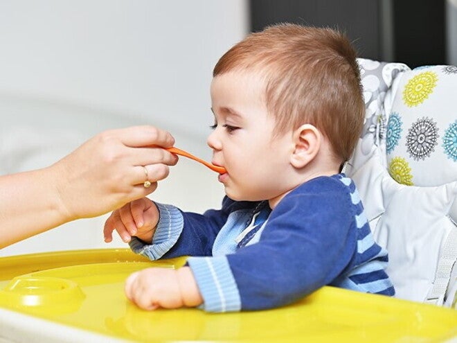 Beneficios de las papillas Bebé sentado en una silla alta siendo alimentado con una cuchara por una mano adulta