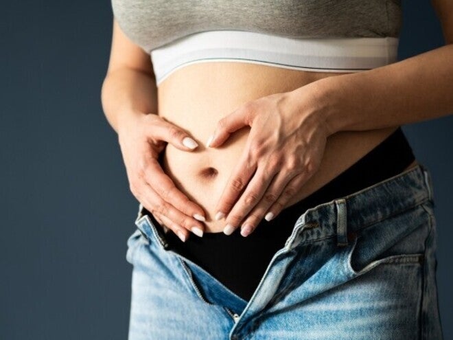 Abdomen de mujer embarazada en primer o segundo trimestre, manos en forma de corazón sobre el vientre.