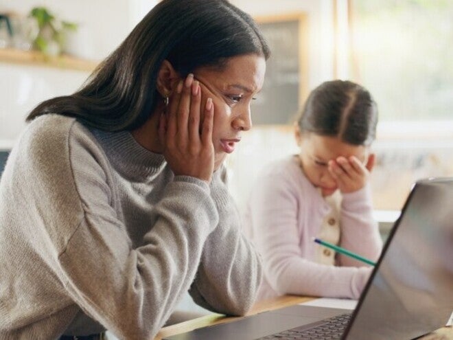 Madre y niña sentadas en la mesa de la cocina con una computadora portátil, realizando una actividad escolar en casa.