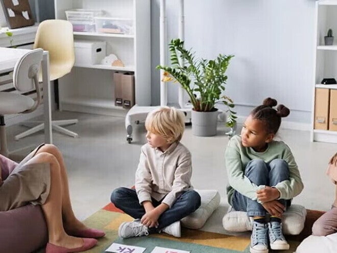 ¿Qué es la Apraxia del Habla Infantil? Patólogo del habla y lenguaje, SLP terapeuta del habla y lenguaje, fonoaudiólogo mostrando abecedario a niños pequeños sentados sobre cojines.