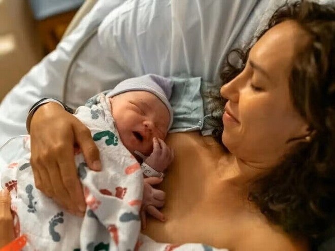 Mamá abrazando a su bebé en una cama de hospital luego de un parto por cesárea