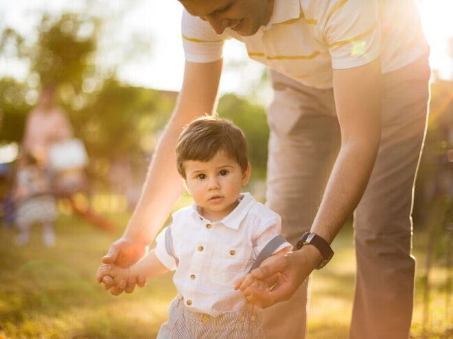 Consejos para estimular los primeros pasos del bebé Adulto ayudando a un niño pequeño a caminar.