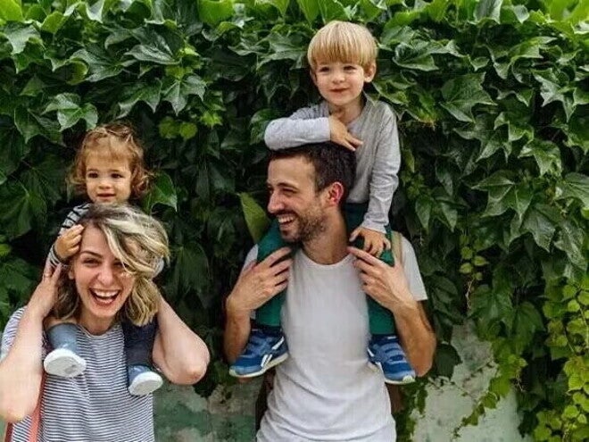 Crianza consciente y respetuosa Dos adultos con dos niños sobre sus hombros, frente a una pared cubierta de hojas.