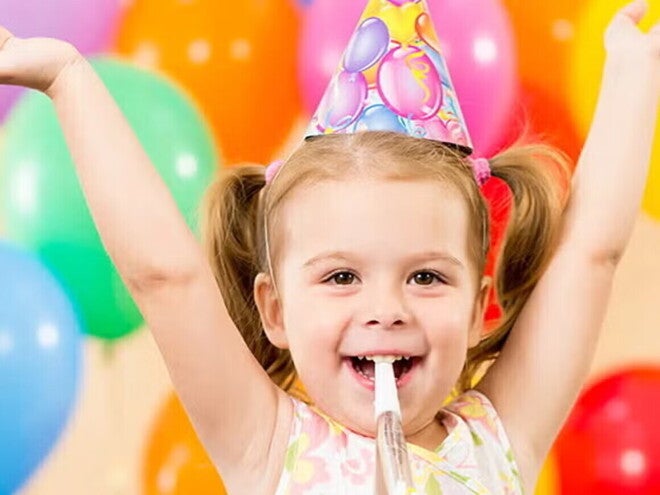 Guía para fiestas infantiles Niña pequeña feliz en una fiesta infantil con globos de colores.