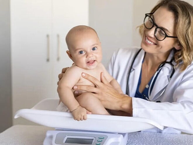 Doctora sonriendo y pesando a un bebé feliz.