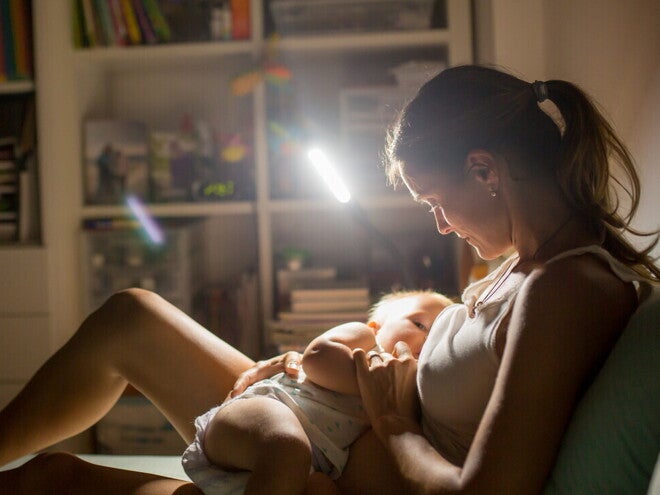 Mamá sentada en el sofá amamantando a su bebé de noche.