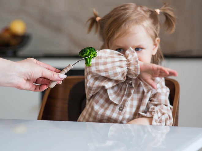 Mamá está alimentando a una niña brócoli con cuchara. La bebé se niega a comer. 