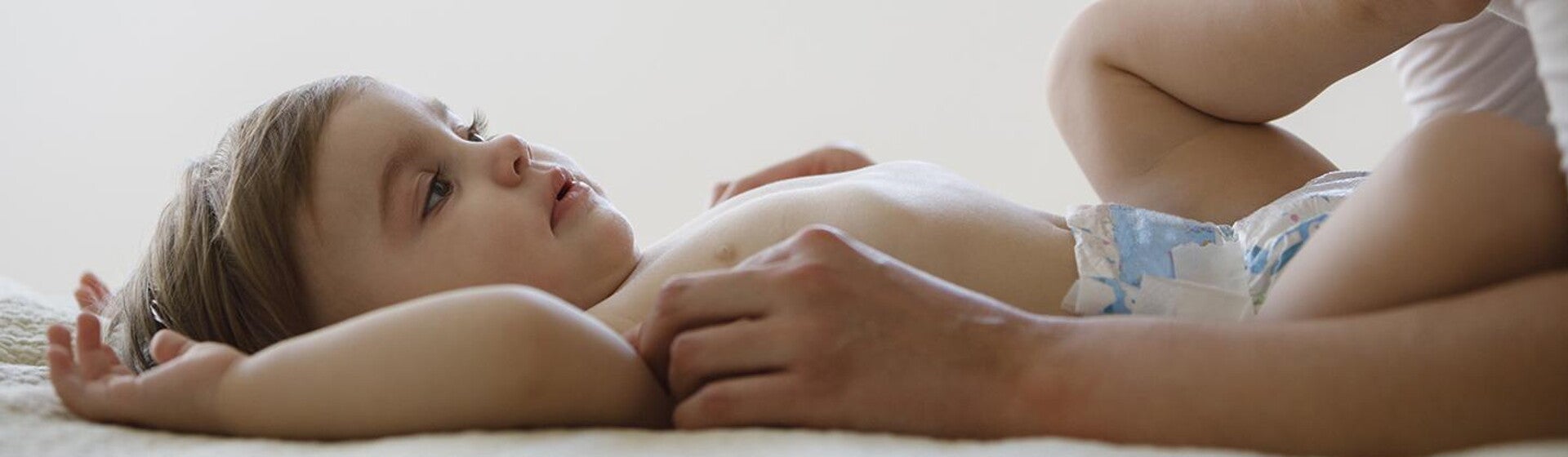 Bebé acostado boca para arriba en pañales, manos de mamá lo acarician.