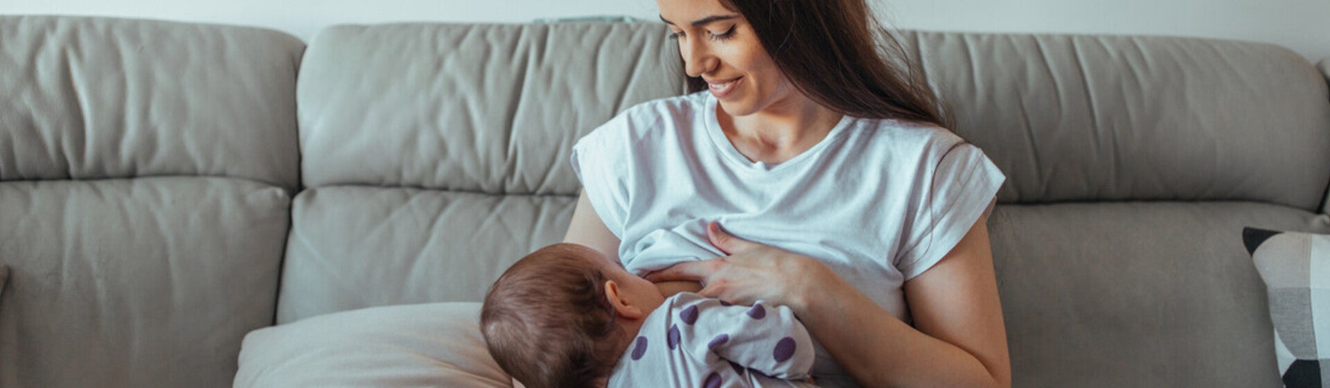 Mamá sentada en un sofá sonriendo, amamantando a su bebé. Lactancia materna.
