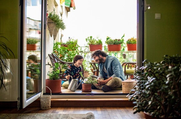Padre e hijo sonriendo, sentados en el piso, regando plantas con una regadora.