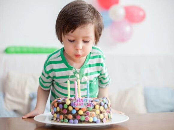 Cumpleaños infantil Niño pequeño soplando las velas de un pastel de cumpleaños en una sala decorada con globos.