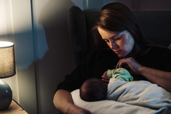 Mamá sentada dando de mamar a su bebé, con rostro preocupado.