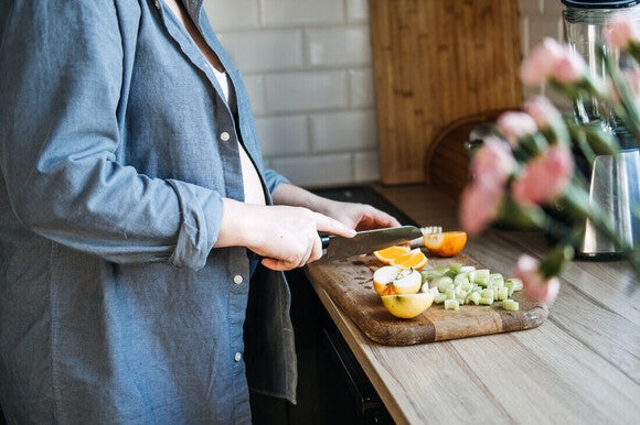 Mujer embarazada cortando frutas con nutrientes clave para el embarazo como vitamina C y ácido fólico